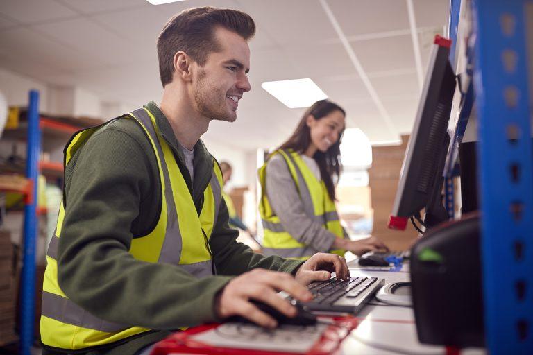 Staff In Busy Modern Warehouse Working On Computer Terminals