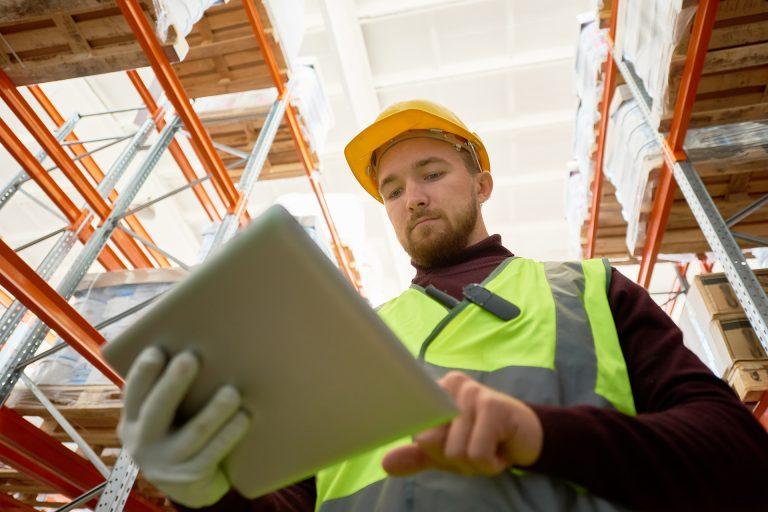 Low angle portrait of warehouse worker holding digital tablet  while doing stock inventory, copy space